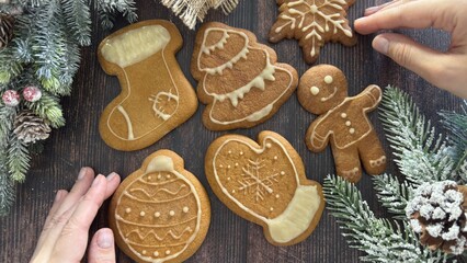 Hands lay out gingerbread cookies on the table, surrounded by a festive tree