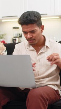 Indian man at home struggles to read tiny text on laptop then puts on glasses and sees clear view. Arabian guy on sofa smiles adjusts frame reads screen lines without strain and continues work task.