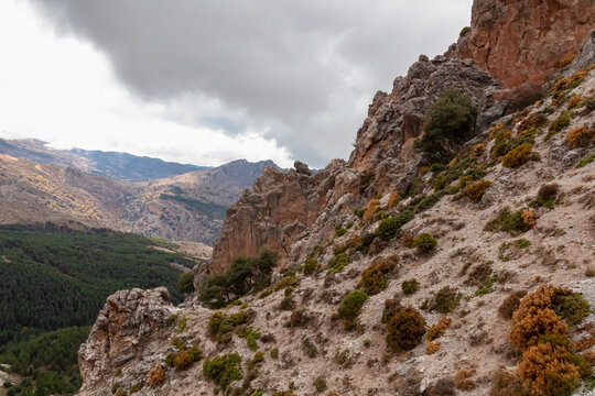 Jagged limestone cliffs rise dramatically above a deep valley under a cloudy sky, highlighting the raw beauty and rugged terrain of the Sierra Nevada National Park in Andalusia, Spain.