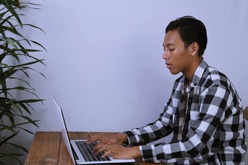 Young Gen Z man working remotely at home, thinking and focusing on tasks using laptop. Authentic daily life, modern lifestyle, and digital work concept.