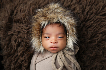 Funny amusing portrait of an androgynous neutral newborn baby boy or girl in a fur hat with humorous irritated expression of incredulity, animosity, irritation, hostility, annoyance or indignation
