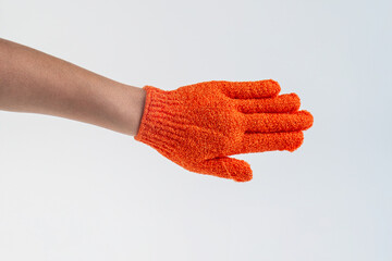 An orange exfoliating glove in a hand against a white background.