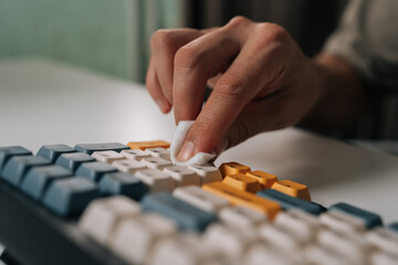 Person cleaning and maintaining wireless mechanical keyboard, ensuring hygiene and clean workspace for computing and technology device care. Concept of service, cleaning computer equipment.