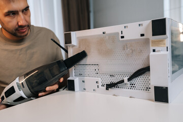 Focused man cleaning computer system unit with vacuum cleaner, removing dust from dirty air filter and mesh panel, providing essential pc maintenance and hardware care for optimal performance.