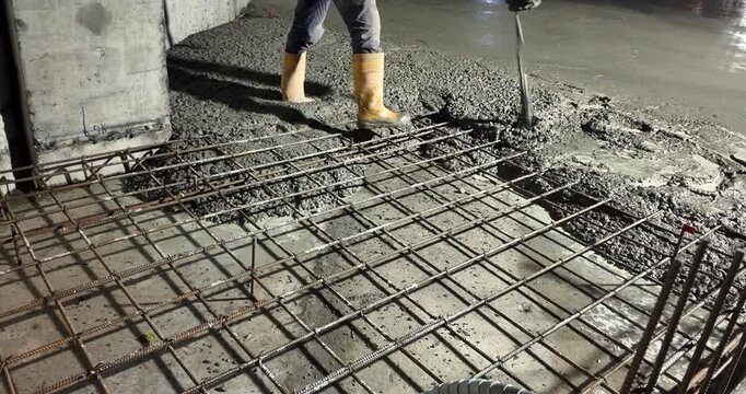 close up of a construction worker pouring concrete onto a rebar grid at night.