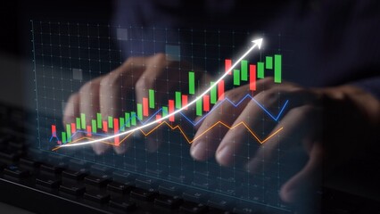 Close-up of hands typing on a keyboard with digital financial graphs displayed on screen, illustrating significant growth and market analysis in a modern workspace. Copula