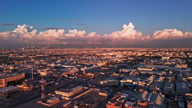 Wide drone view toward Kuwait City: golden-hour light, towering cumulonimbus line, coastal horizon, dense residential grid, highways, pylons, and warehouses&mdash;clean establishing shot for travel .