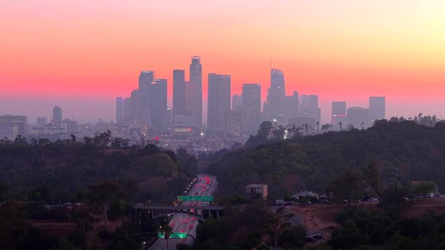 Downtown Los Angeles California, city skyline at sunset with traffic flowing along Highway toward city buildings. Highway 110. Timelapse of cars driving in traffic towards beautiful evening sunset.