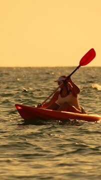 Kayaking woman paddles aggressively at sunset on the ocean water during golden hour sports activity Vertical video.