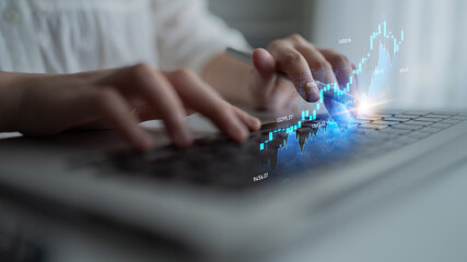 A close-up of hands typing on a laptop is surrounded by glowing stock market data and financial...