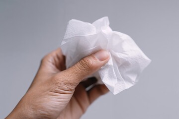 Human hand holding white tissue against neutral background