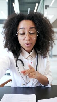 POV Vertical. Smiling African American talking on video call using phone in hospital clinic. Medical worker physician is having a remote online consultation with a patient in office looking at camera