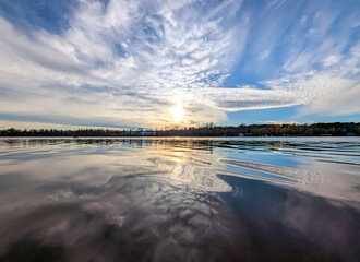 Pastel and blue clouds float magically over the river at sunset. Panorama of calm evening fluffy sky above the water. Reflected mirror in the water, enjoying cloud nature evening yellow sun.