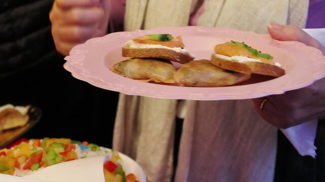 Invit&eacute;e tenant une assiette avec toasts et samoussas lors d&rsquo;un anniversaire, moment convivial autour d&rsquo;un buffet festif
