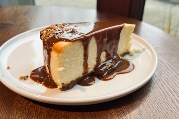 Thick slice of baked cheesecake with salted caramel topping and crunchy garnish, presented on a plate with dramatic natural lighting.