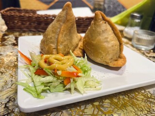 Traditional samosas with flaky crust and aromatic filling, served with dipping sauces on a rectangular plate, perfect for lunch or snack concept.