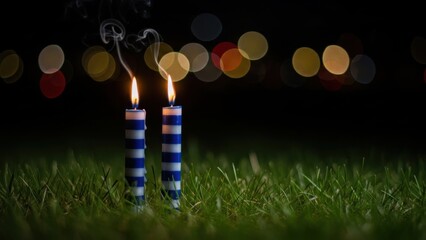 Two blue and white striped candles burning brightly in green grass at night
