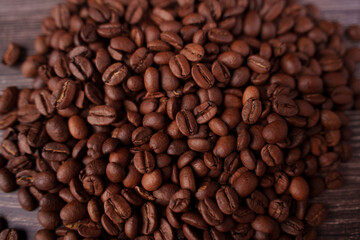 Obraz premium close-up of a vibrant pile of roasted coffee beans with various shades of brown creating a rich and inviting texture against a rustic wooden surface, highlighting the aroma and warmth of fresh coffee