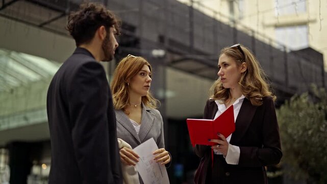 Business people engage in a focused discussion outside a modern office building. They are collaborating on a project, showcasing the flexibility of remote work and effective team communication.