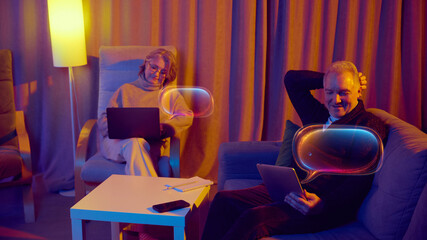 Elderly couple relaxing at home while using digital assistants on tablets. Concept of tech promotion, senior digital services, retirement wellbeing platforms, and user friendly interfaces.