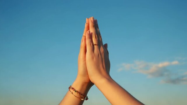 Hands in Prayer Gesture Against Clear Blue Sky at Sunset