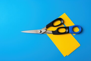 Scissors are cutting yellow paper on a vibrant blue background, creating a crafting activity