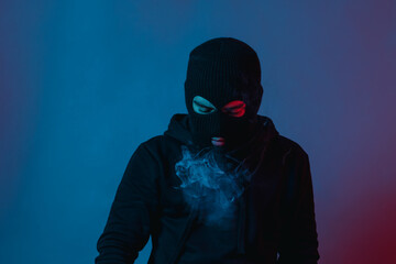 man in hoodie and balaclava looking down and blow smoke out