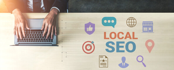 Close-up of hands typing on a laptop on a wooden desk with colorful local SEO icons representing digital marketing and online business strategies. Gantry
