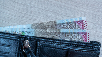 Two 500 Zloty Notes Tucked into Black Leather Wallet on Light Wood
