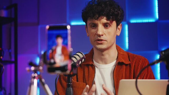 Young male podcast creator recording video on phone, speaking into microphone