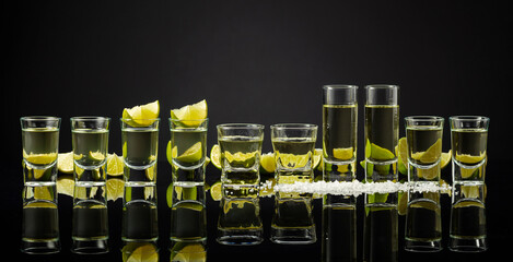 Tequila shots with lime slices and salt on a black reflective background.