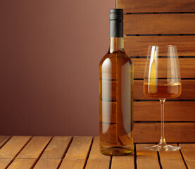 Bottle and glass of white wine on a wooden background.