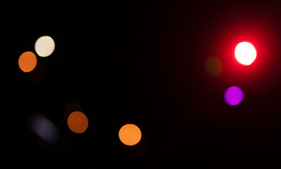 Abstract night bokeh with scattered glowing light circles in red, orange, white, and violet on a