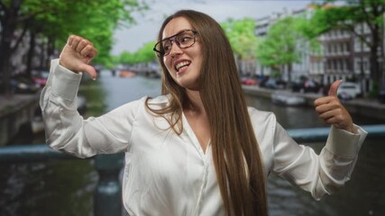 Woman thumbs up with right hand and thumbs down with left on street in amsterdam; playful contradiction.
