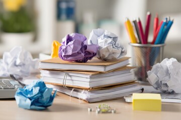 Papers are stacked on a desk with crumpled notes around them. Office supplies sit nearby as work continues in a creative space