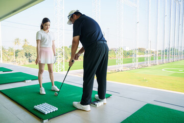 Golf instructor teaching beginner woman at driving range