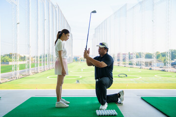 Golf instructor teaching beginner woman at driving range