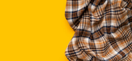 Wrinkled in folds plaid brown orange flannel cotton fabric on yellow background, top view. Autumnal natural fabric for shirt, dress, tablecloth, clothing. Abstract textile background, tartan 