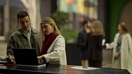 Two business professionals are engaged in a collaborative discussion while working on a laptop.