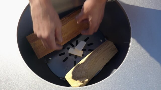 Hands placing fire starter and logs inside a modern fire pit, showing outdoor setup and efficient ignition