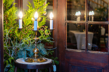 Brass Christmas candelabrum with lit candles by wooden window surrounded by evergreen branches...