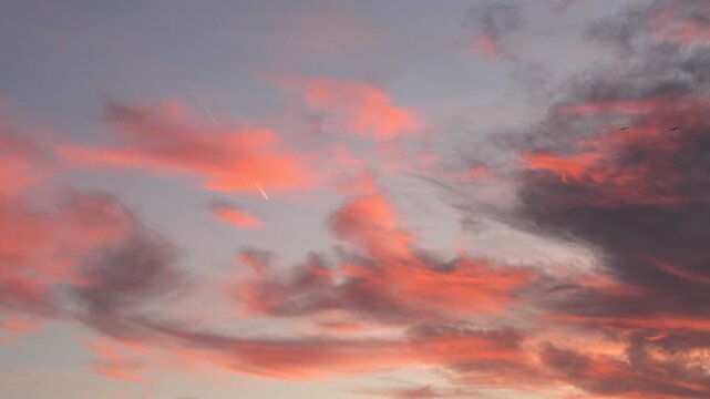 A plane flies through a colorful sky filled with pink and gray clouds during sunset. The scene captures the beauty of aviation and nature.