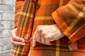  A woman buttoning her coat, close-up. A woman unbuttons her coat. women's fingers fastening a button. woman putting on coat. fingers fasten a button. autumn coat. warm clothes