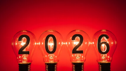 Four illuminated light bulbs with numbers forming the year 2026 on a bright red background with a gradient effect