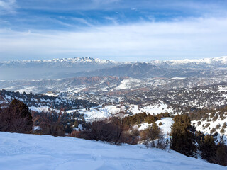 Panoramic view of snow-covered mountains at Amirsoy ski resort, Uzbekistan. Winter landscape with mountain range and blue sky, travel and nature