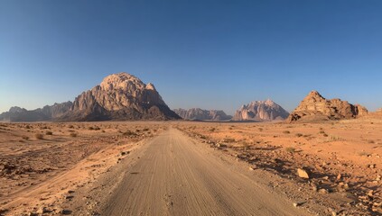 Naklejka premium A vast desert landscape, a dirt road stretching toward distant mountains under a clear blue sky