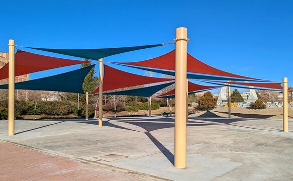 Parasoles triangulares de exterior, de color rojo y azul, sostenidos por postes en plaza p&uacute;blica 