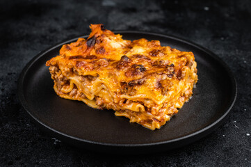 Classic Italian lasagna with beef meat sauce pasta layers and melted cheese on black plate overhead copy space