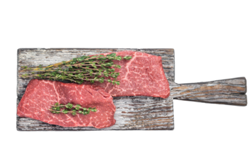 Raw flatiron steaks with thyme on rustic wooden board and carving fork top view on isolated background with copy space