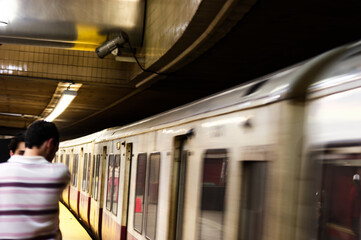 Urban Commute: Man In Striped Shirt Briskly Passing Subway Train on Dim Platform During Rush Hour